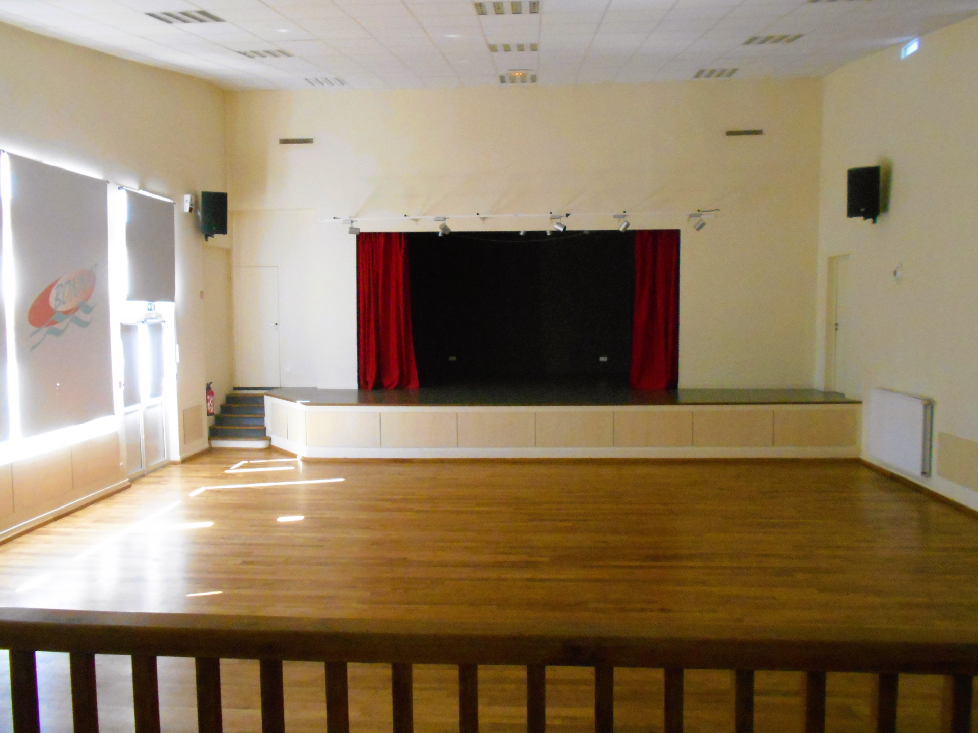 Salle avec scène, rideaux rouges, projecteurs, écran et parquet.