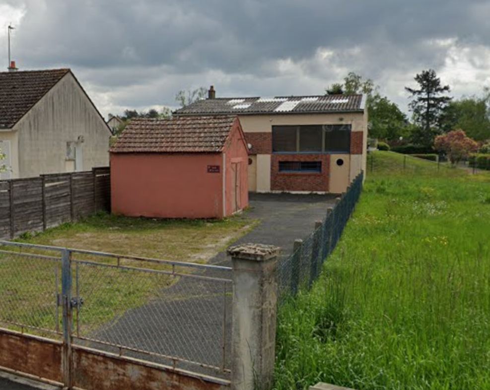 Deux bâtiments, clôture, chemin, terrain herbeux.