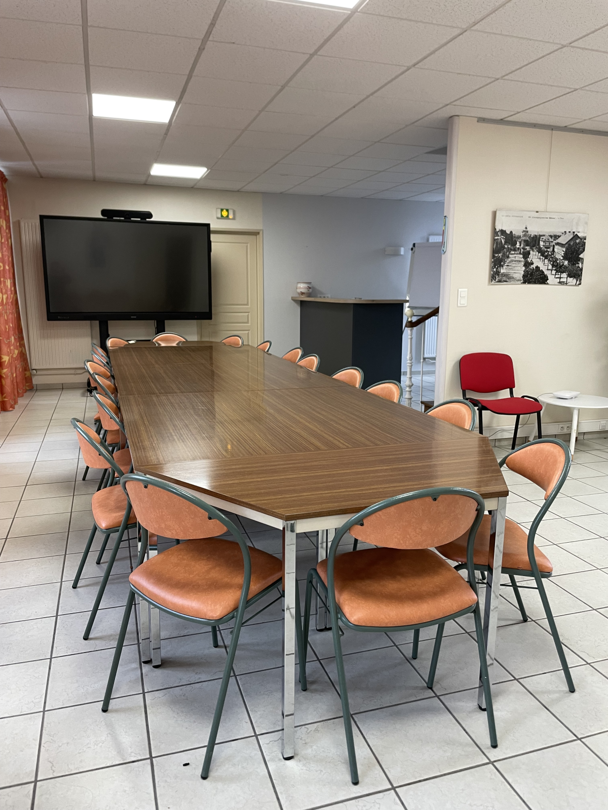 Salle de réunion avec table, chaises, écran, tableau et armoire.