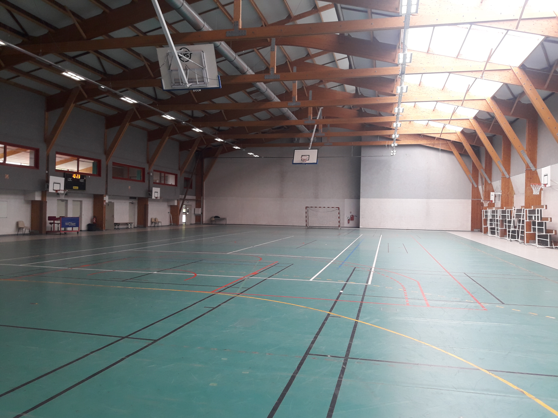 Gymnase avec paniers de basket, filet de volley-ball, gradins et éclairage.