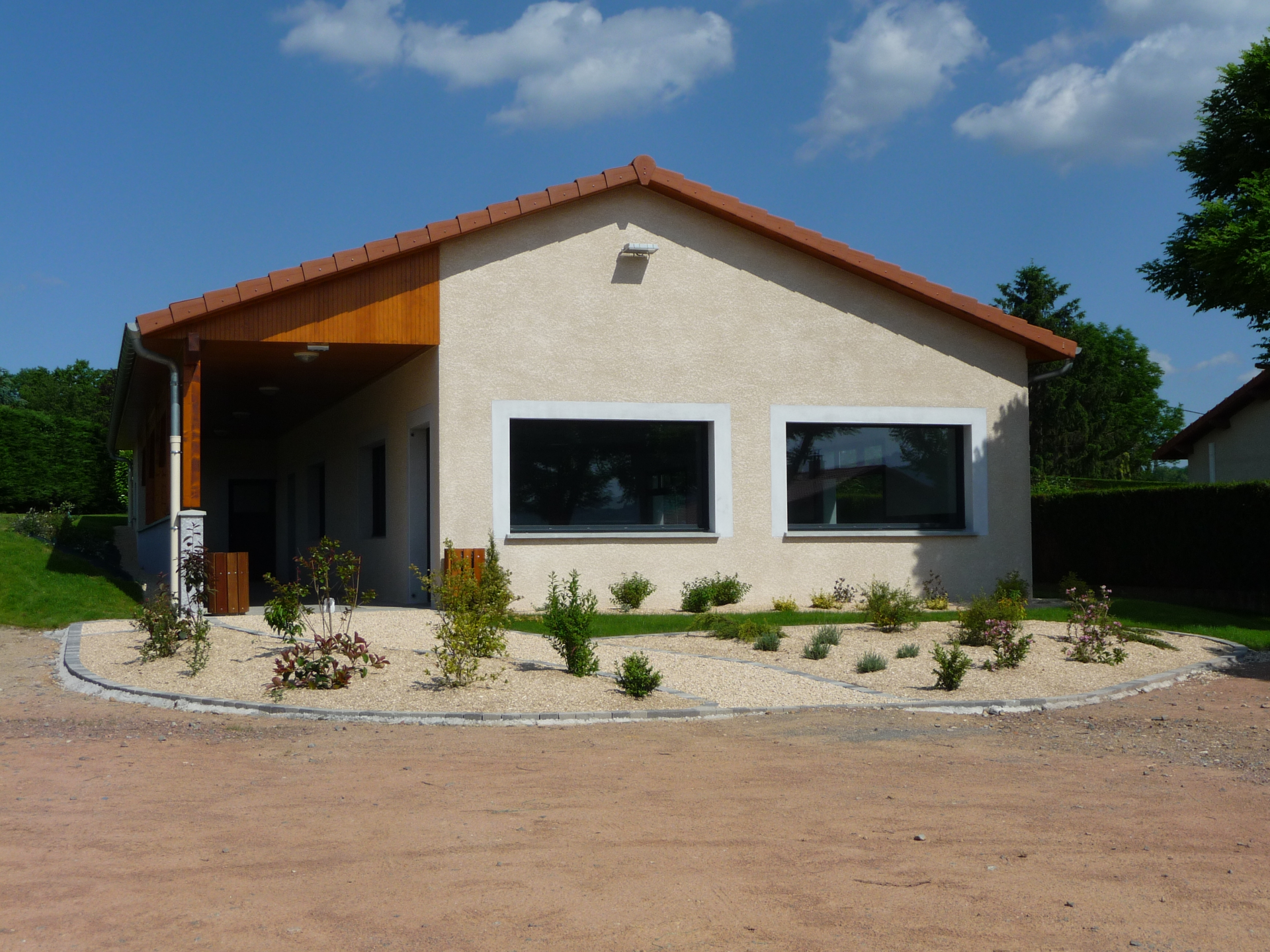 Maison beige avec toit rouge, fenêtres, porte vitrée, allée et plantes.