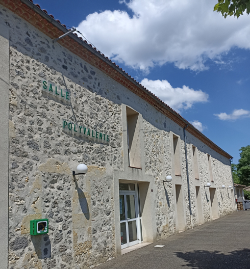 Bâtiment en pierre avec enseigne "salle polyvalente" et réverbère.