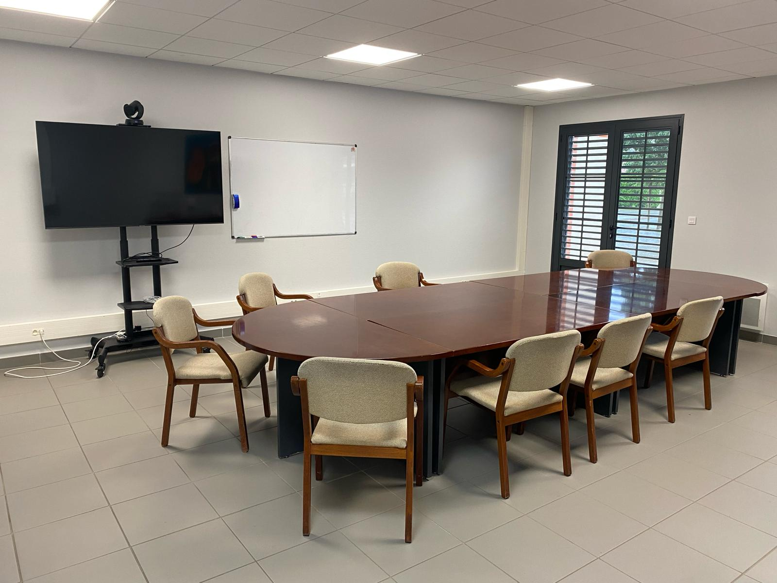 Salle de réunion avec table, chaises, écran, tableau blanc et caméra.