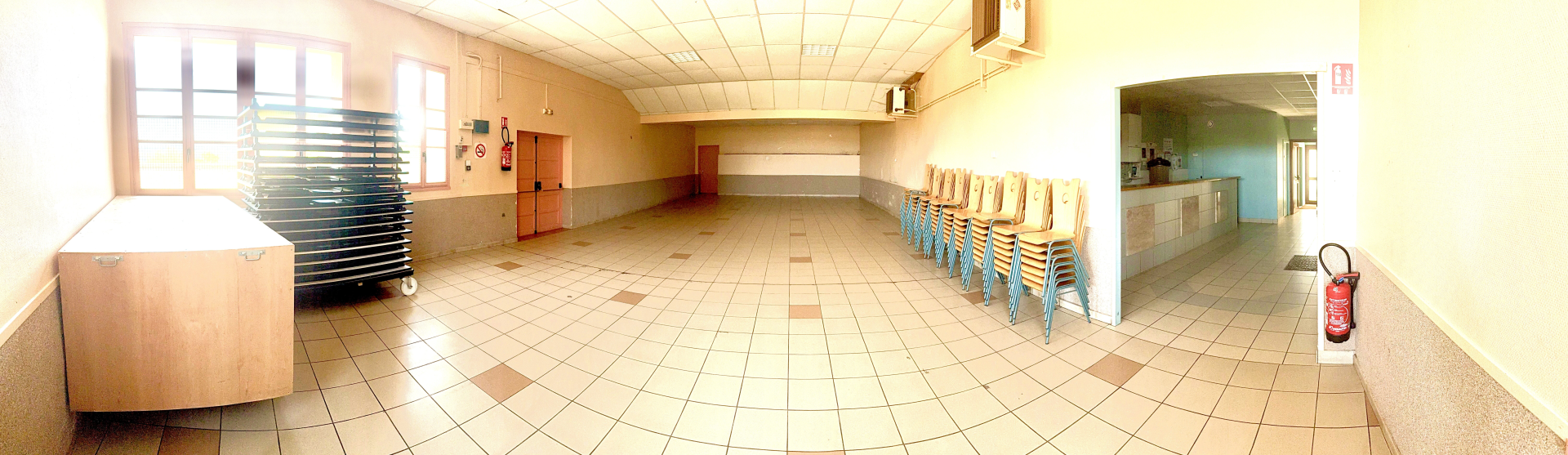 Salle vide avec chaises, table, extincteur, et fenetres avec store.