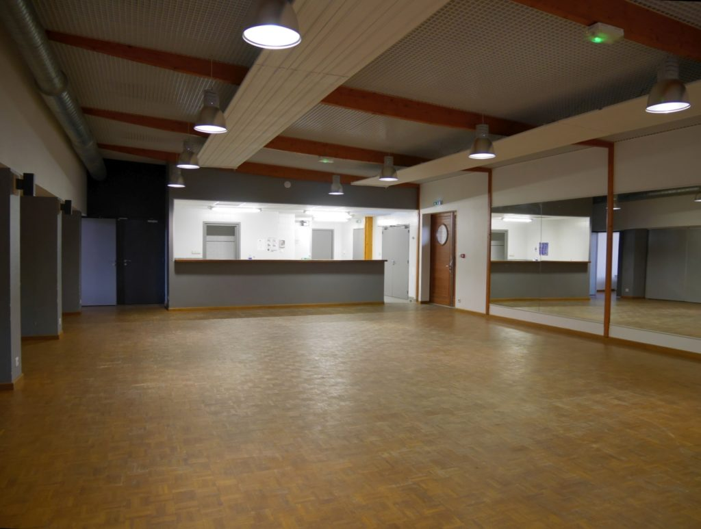 Salle spacieuse avec plancher en bois, comptoir, portes, miroir et éclairage suspendu.