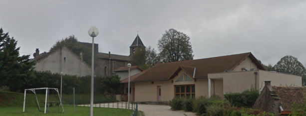 Bâtiment avec toiture marron, clôture blanche, lampadaires, et terrain de football en arrière-plan.