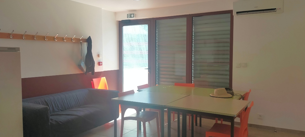 Pièce avec canapé, table, chaises, porte-manteau, climatiseur et porte vitrée.
