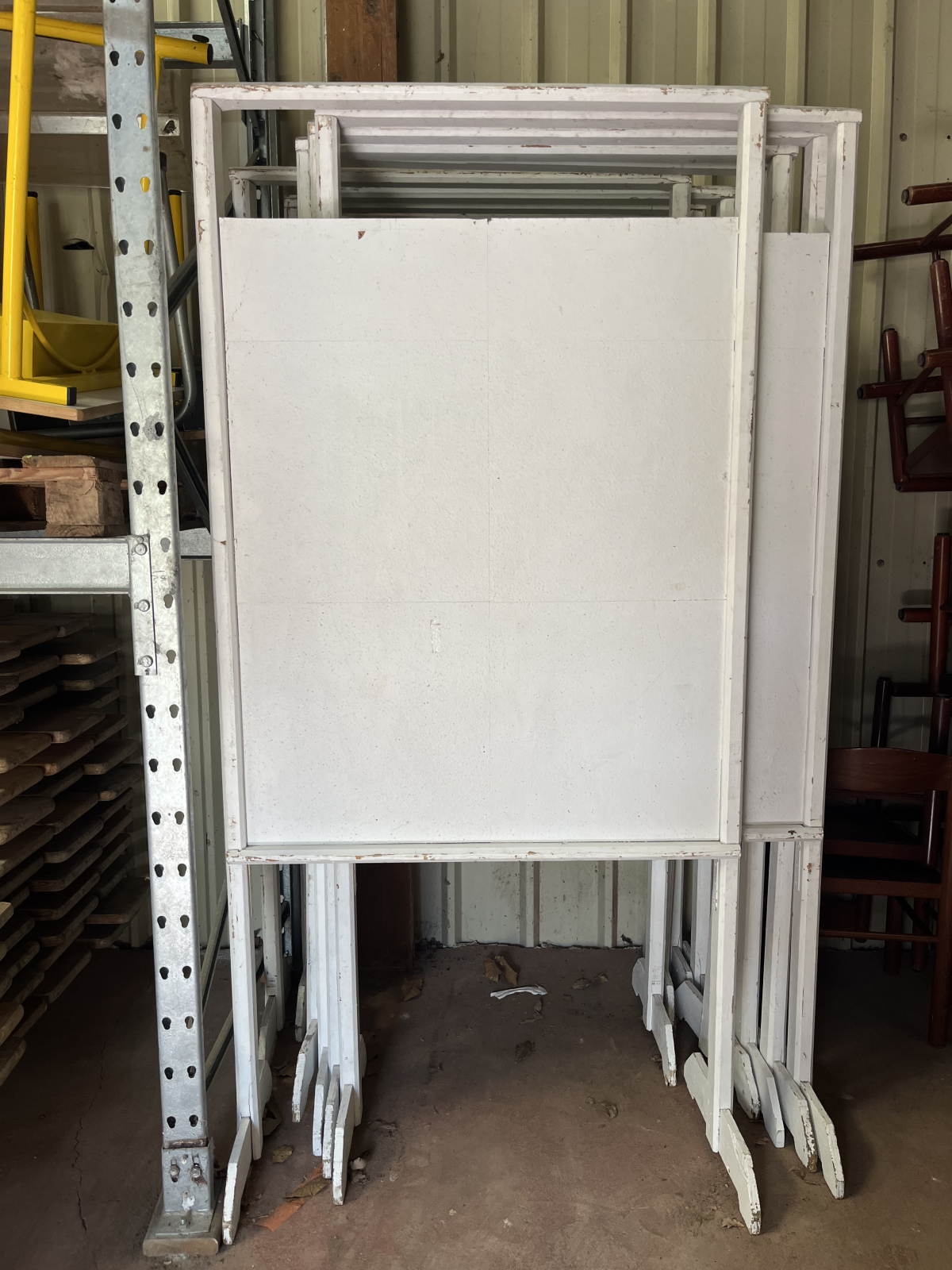 Table pliante blanche avec pieds en métal, rangée contre un rack de stockage.