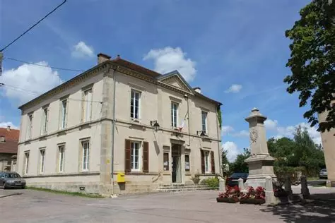 Bâtiment de deux étages avec entrée centrale, fenêtres symétriques, et monument avec horloge devant.