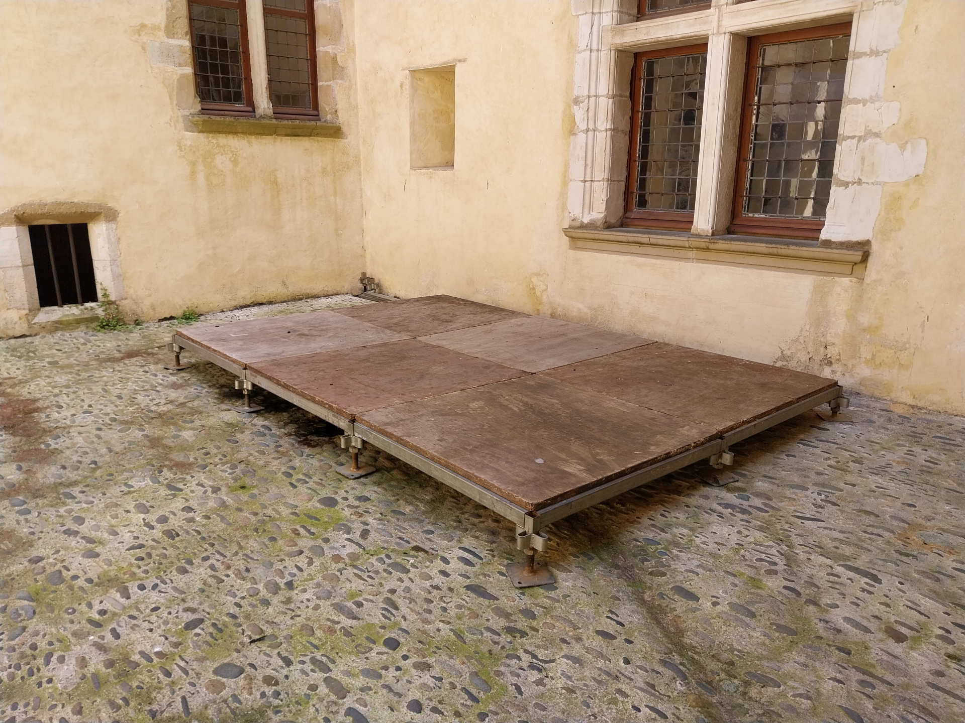 Table en bois sur sol pavé devant un mur avec fenêtres.