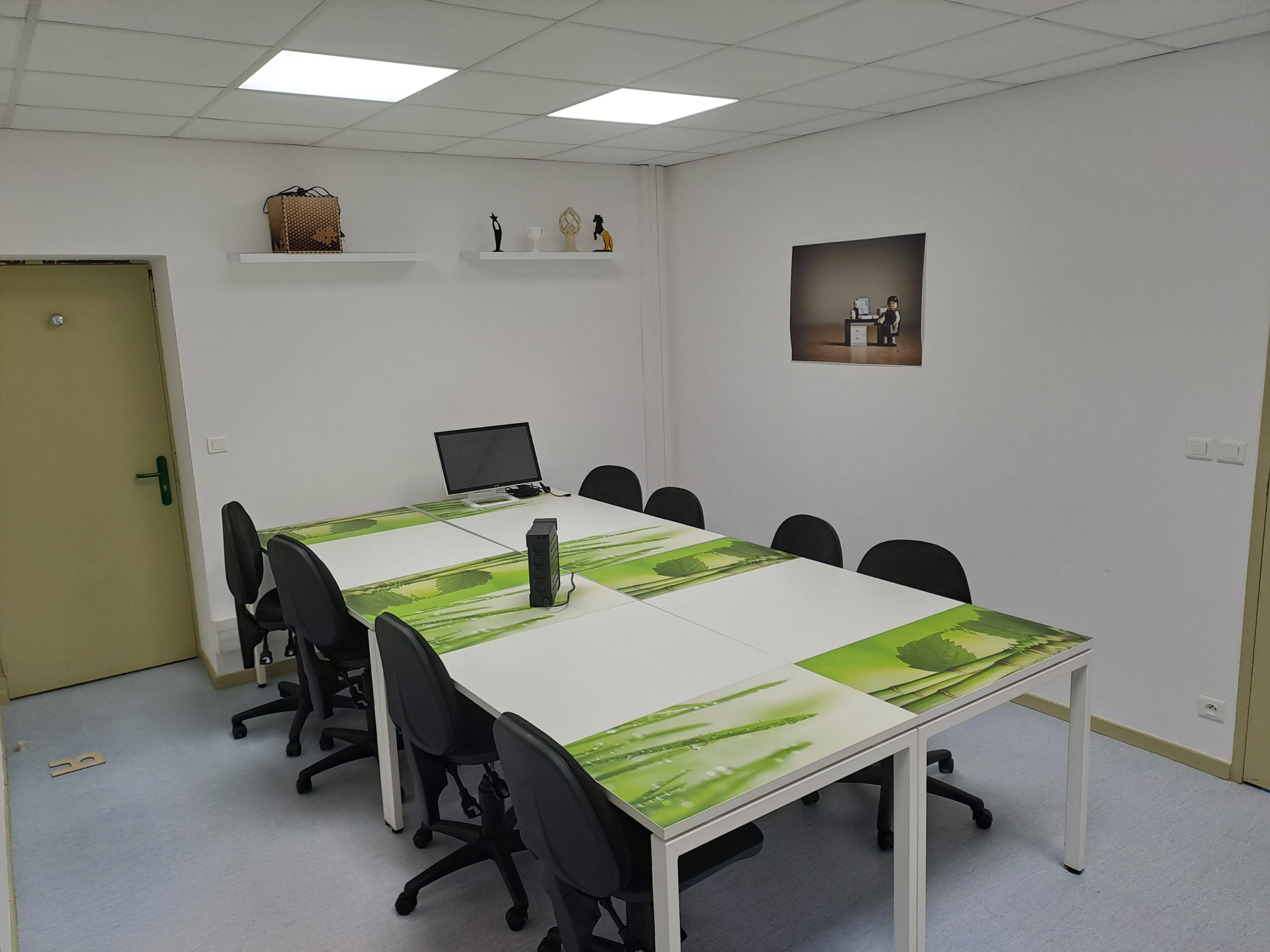 Salle de réunion avec table, chaises, ordinateur, étagères et cadre photo.