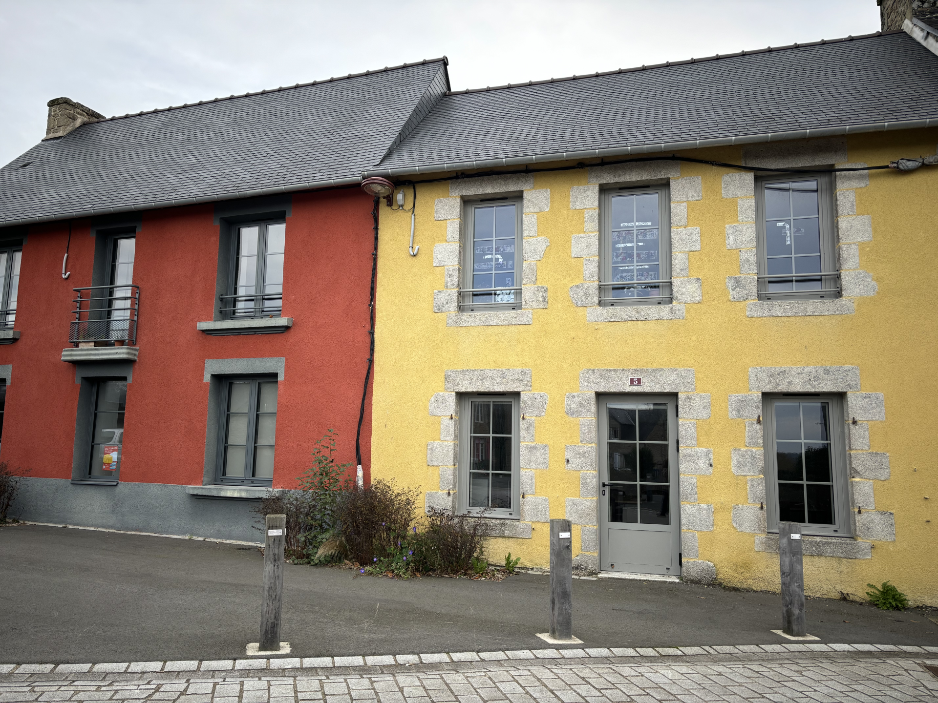 Maison mitoyenne, deux couleurs (rouge et jaune), toit en ardoise, fenêtres avec volets, porte d'entrée.