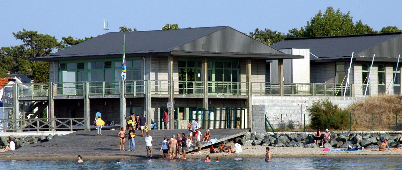 Bâtiment moderne avec balcons, plage, gens, canoës, drapeau.