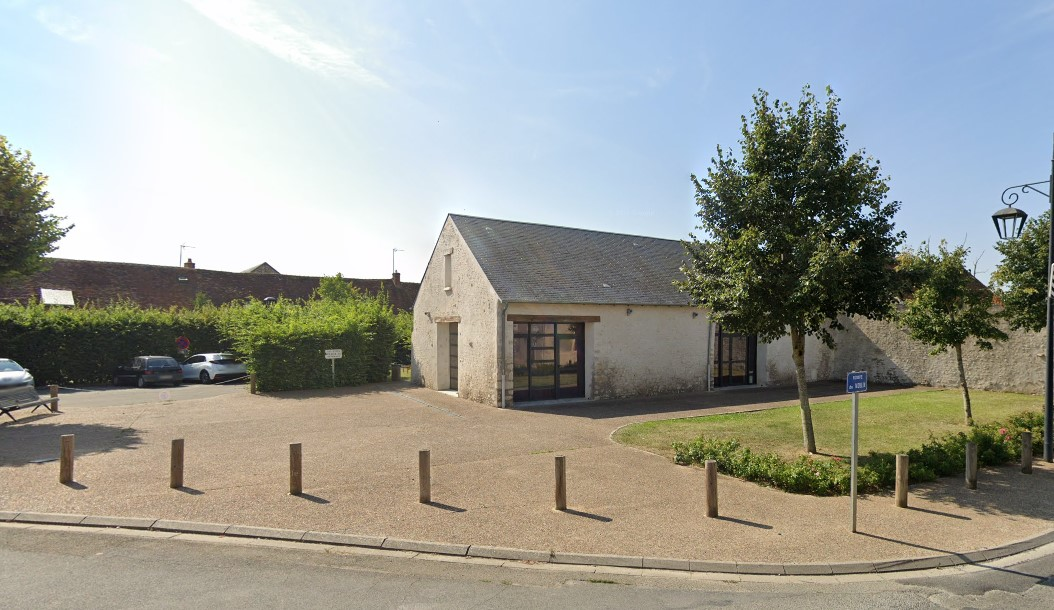 Bâtiment avec parking, buissons, arbre et lampadaire.