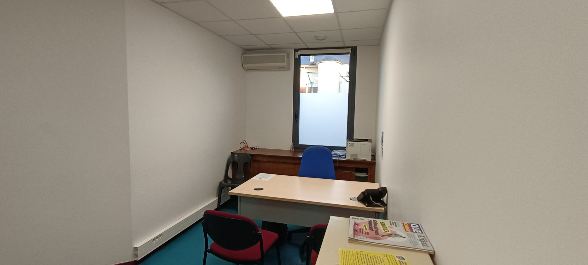 Bureau avec table, chaises, climatiseur, bouilloire, imprimante et documents.