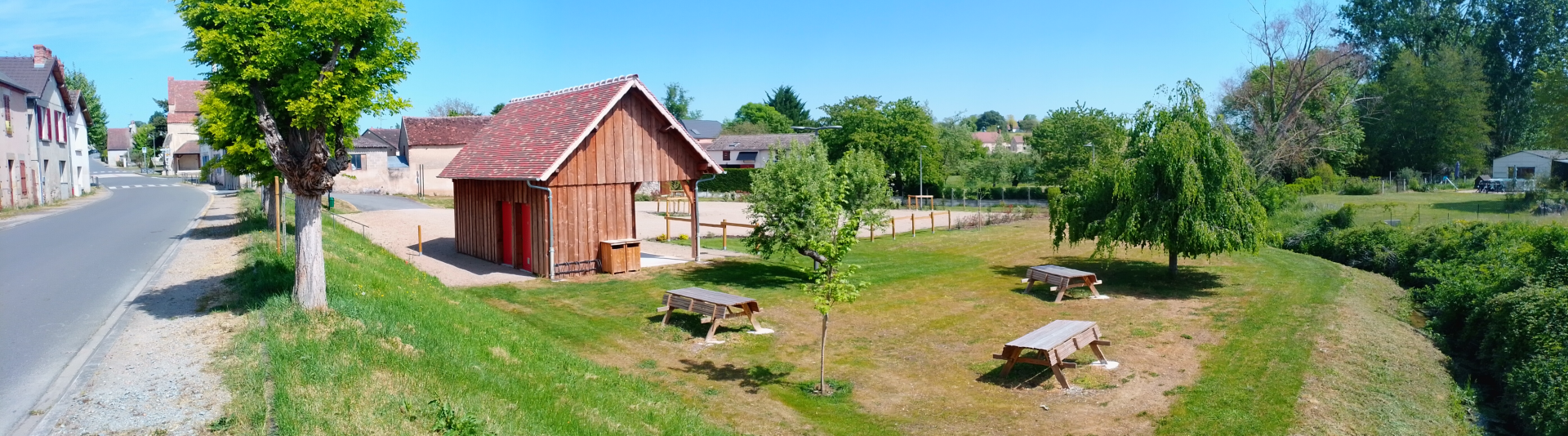 Cabine en bois, tables de pique-nique, arbres, route, maisons.
