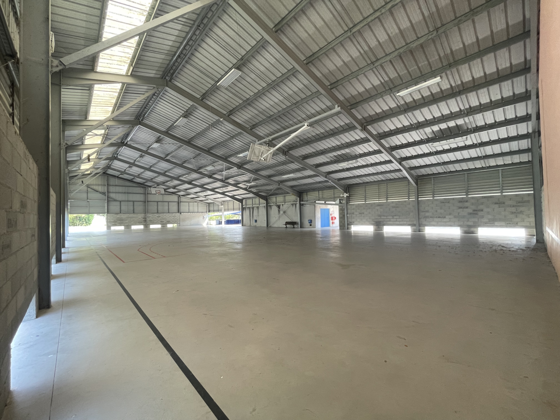 Grand espace vide avec toit métallique, murs en brique, sol en béton.