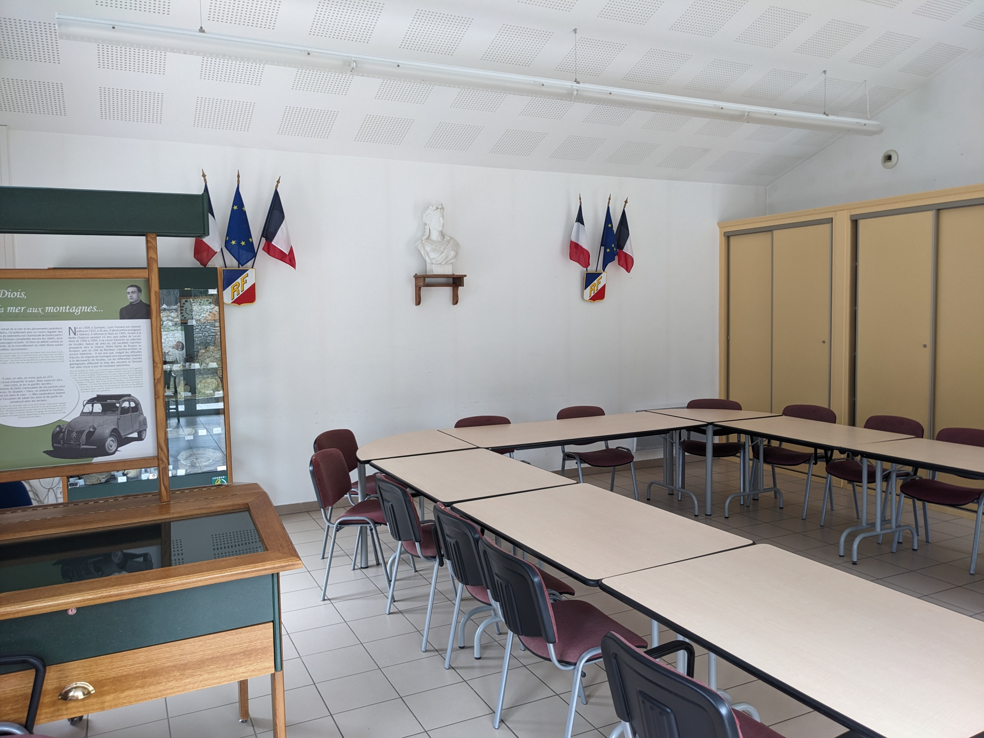 Salle de classe avec tables, chaises, tableau et affichages muraux.