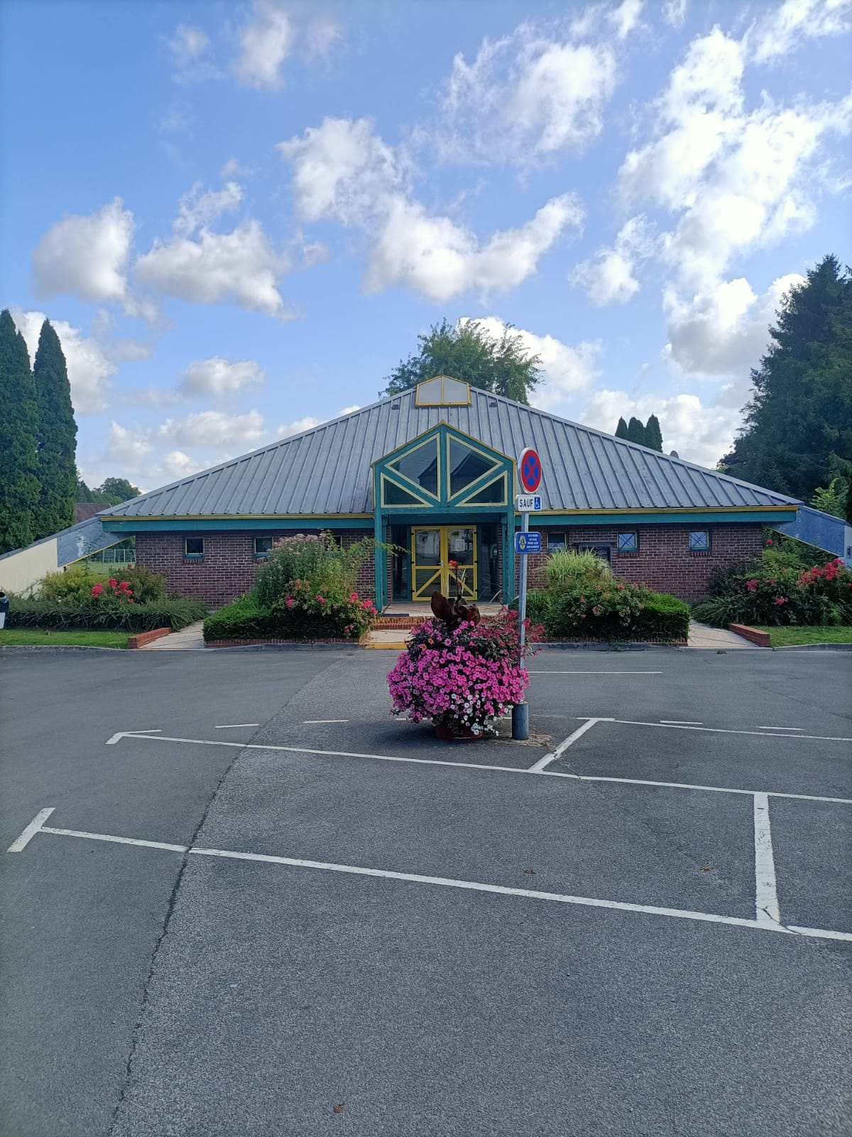 Bâtiment avec parking, fleurs, panneau "arrêt" et "handicapé".
