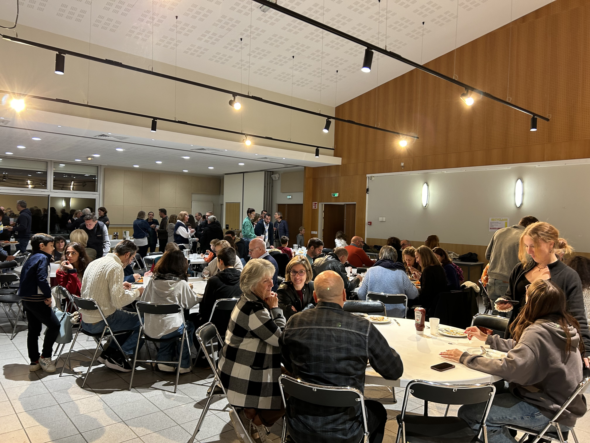 Salle de réception avec tables, chaises, et personnes assises et debout.