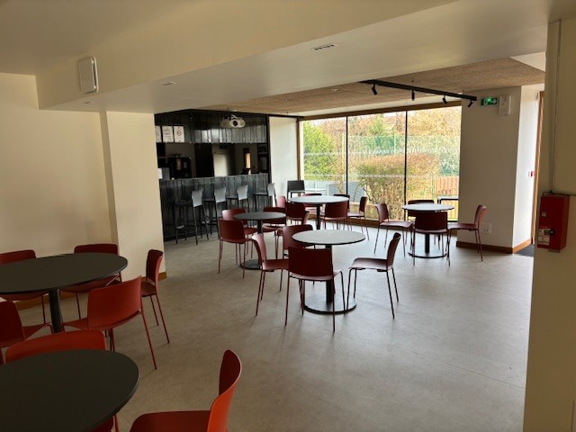 Salle avec tables rondes, chaises, comptoir et distributeur automatique.