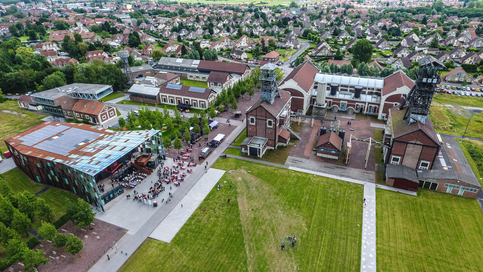 Vue aérienne d'un site industriel avec bâtiments, cheminées, et espace vert.