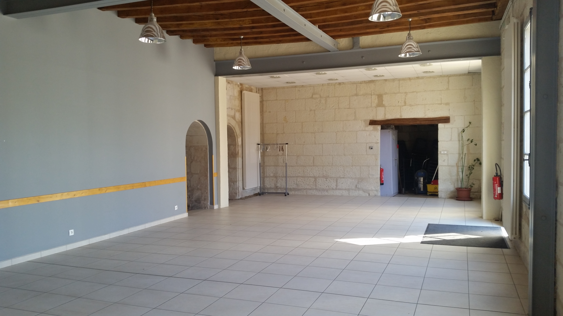 Salle vide avec porte, mur en pierre, porte-manteau, extincteurs et seuil de porte.