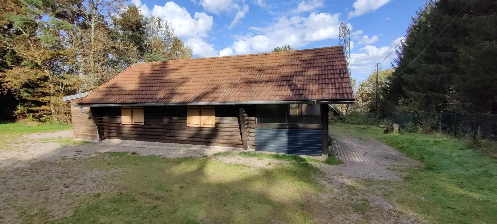 Bâtiment en bois avec toiture en tuiles, porte en métal et arbre derrière.