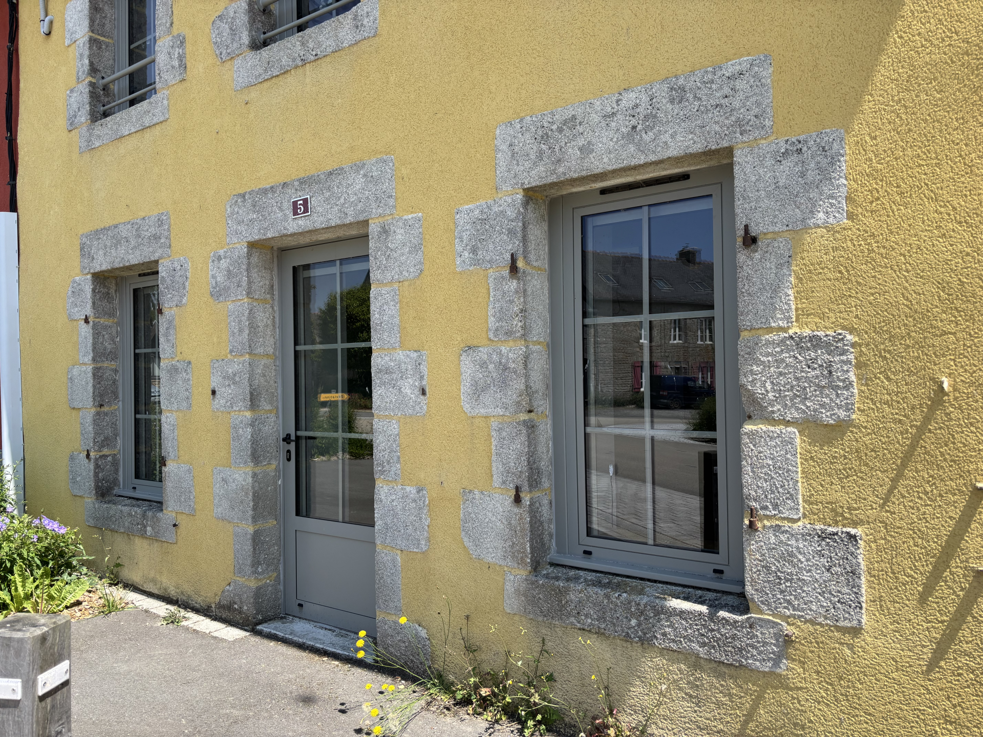 Maison jaune avec porte et fenêtres à encadrement pierreux gris.