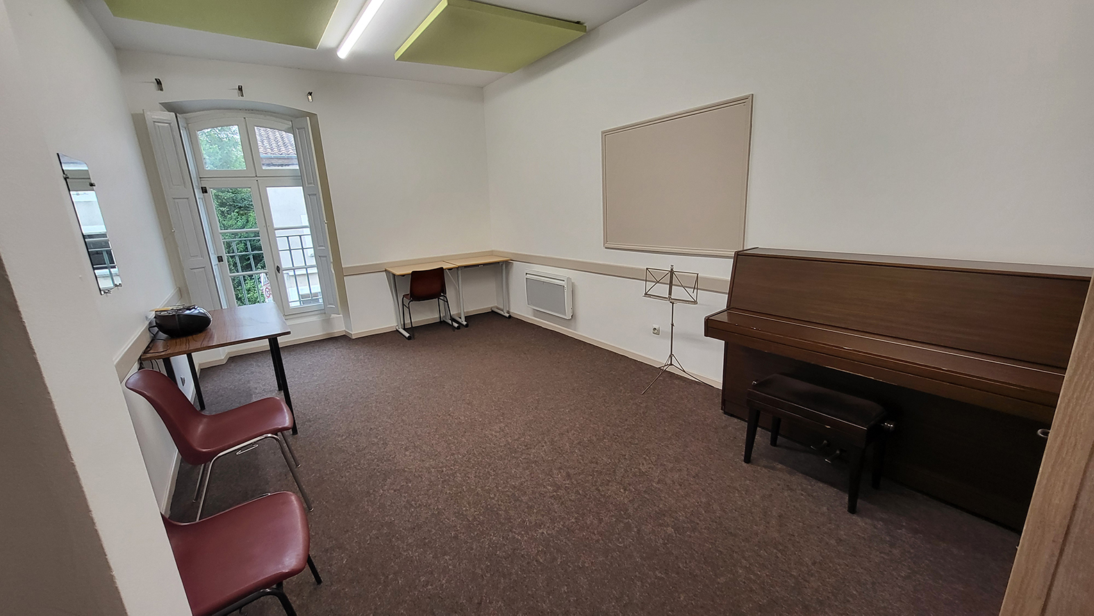 Salle avec piano, pupitre, table, chaises et porte vitrée.
