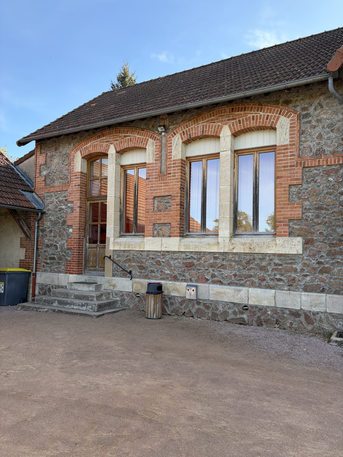 Bâtiment en brique avec grandes fenêtres, escalier extérieur et poubelle.