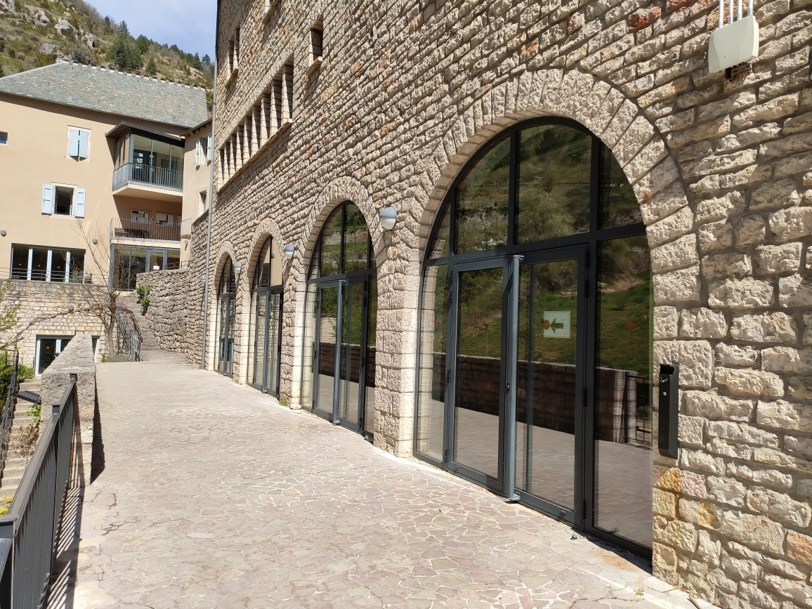"Bâtiment en pierre avec grandes fenêtres arquées, porte en verre et balcon en pierre."