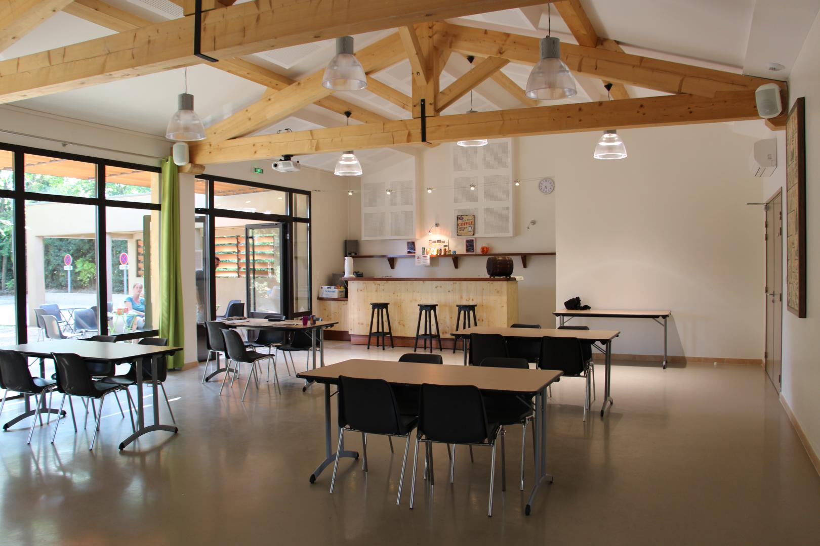 Salle avec tables, chaises, tabourets, comptoir, horloge, luminaires suspendus, porte et fenêtres.