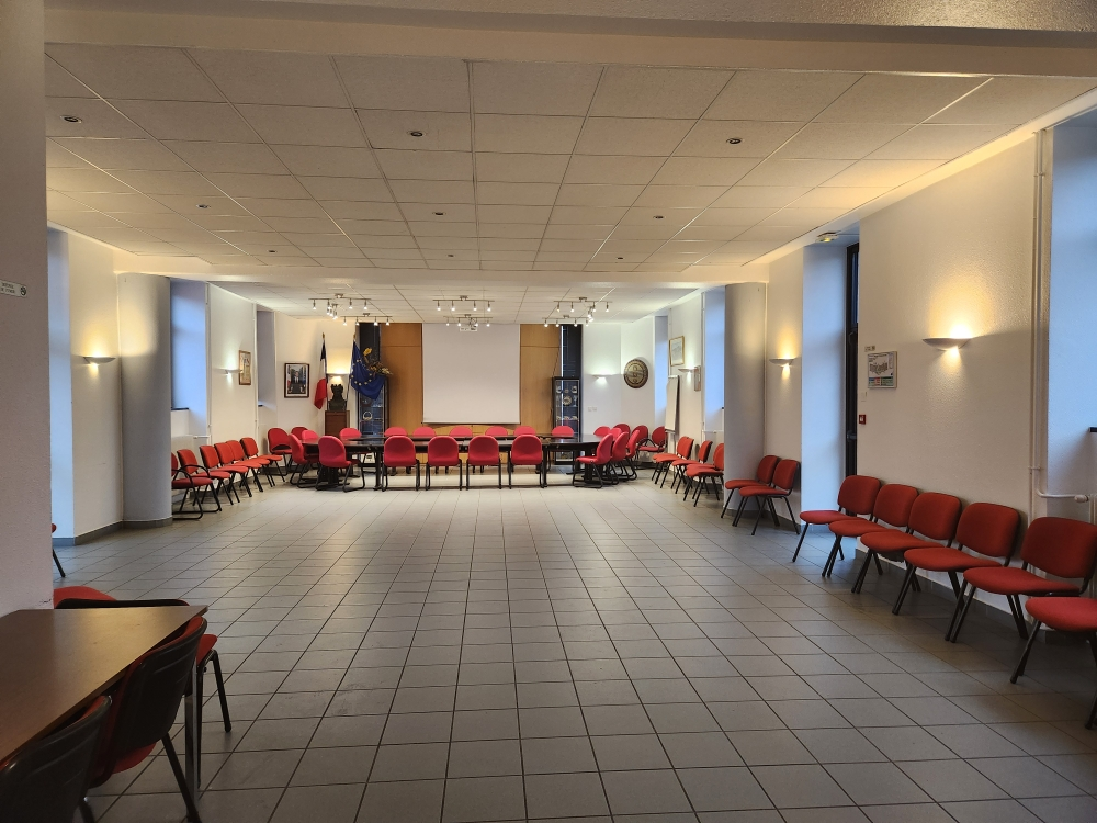 Salle de réunion avec tables, chaises, tableau, éclairage mural et plafonnier.