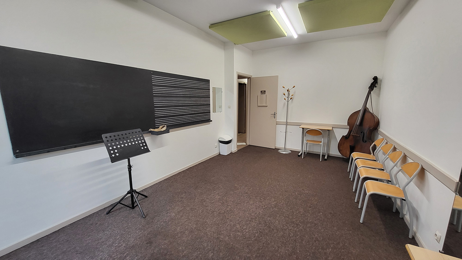 Salle de musique avec tableau, pupitre, chaises, bureau et instrument.