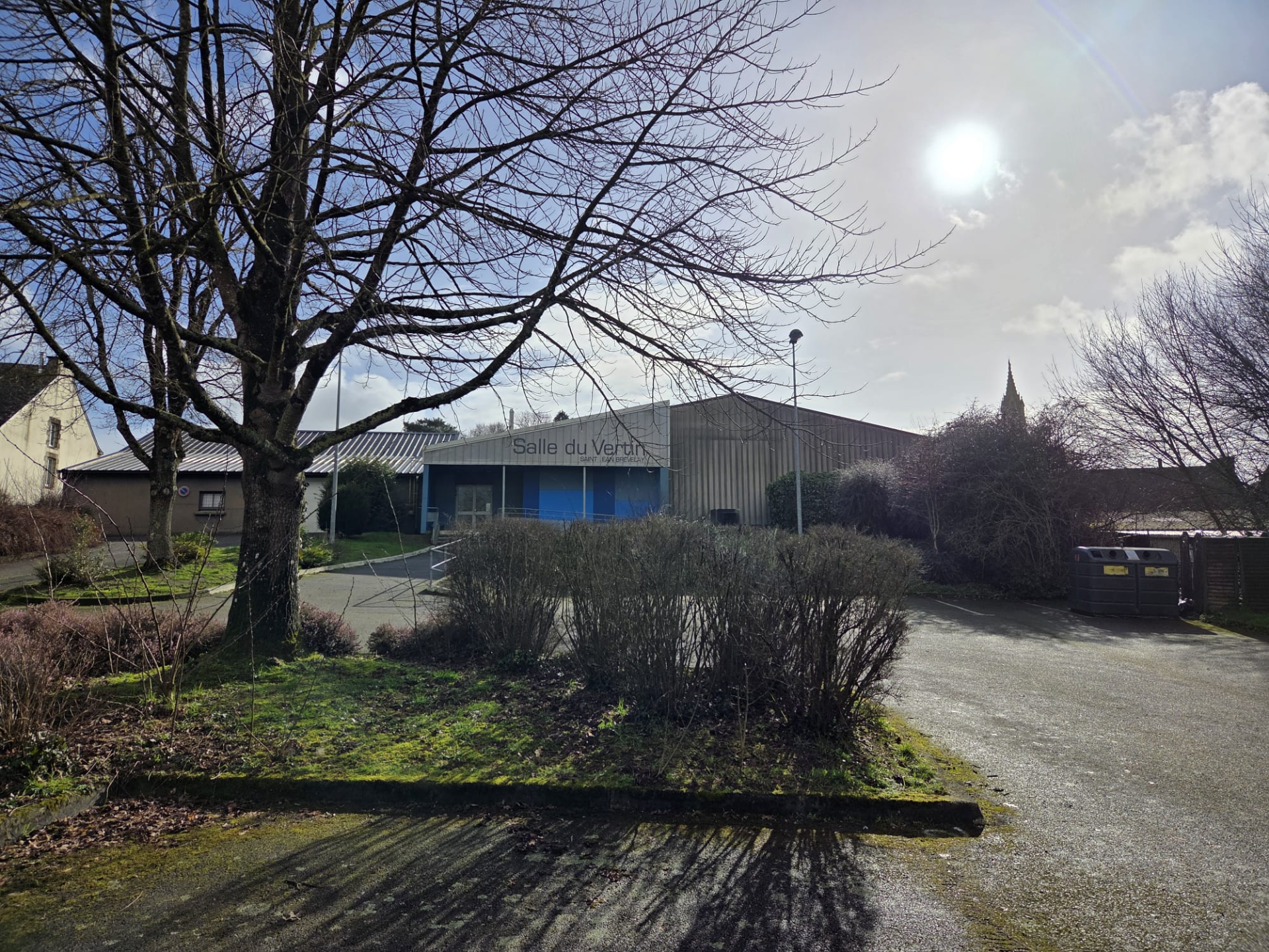 Bâtiment avec enseigne "Salle du Jeu", parking, arbre et buissons.
