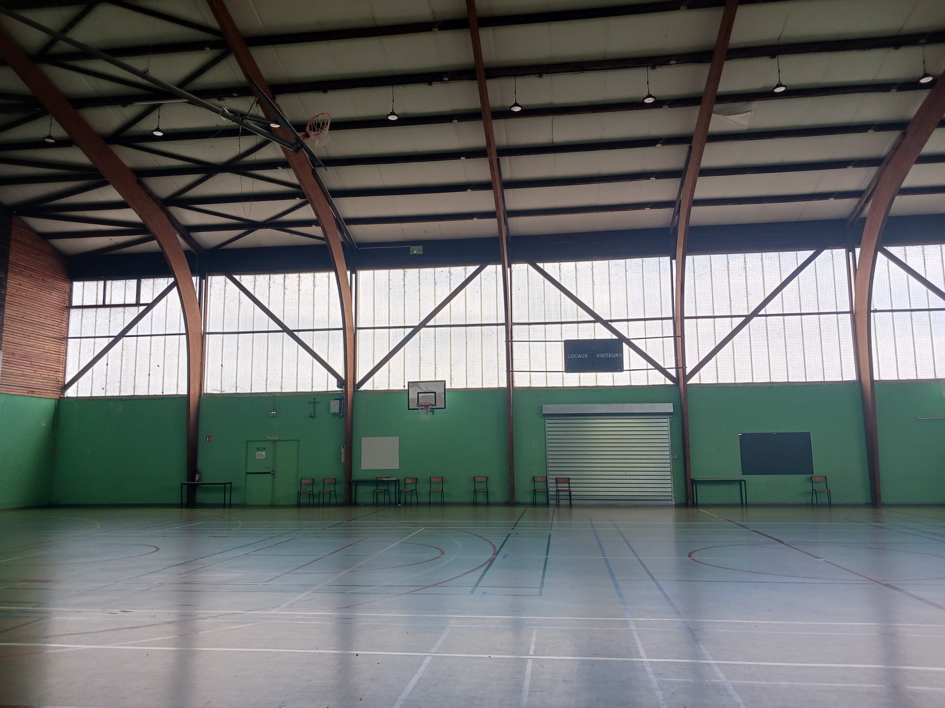 Gymnase avec paniers de basket, tableau blanc, bancs et porte de garage.
