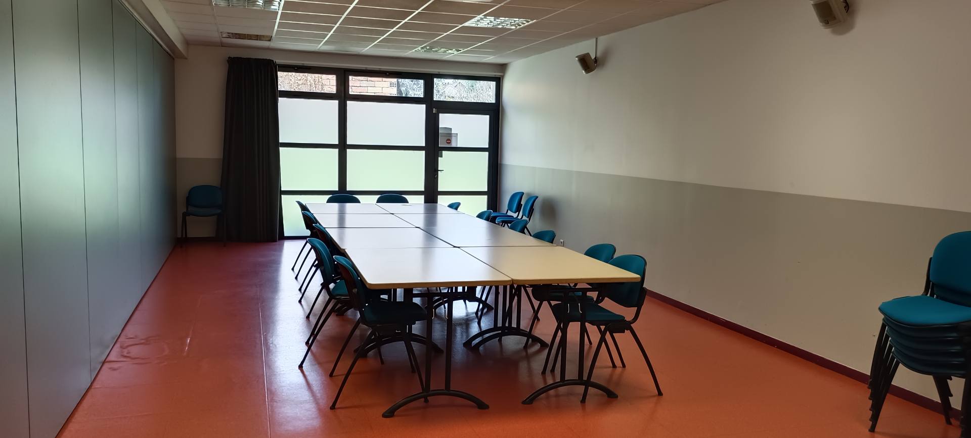 Salle avec table, chaises, fenêtres et porte.