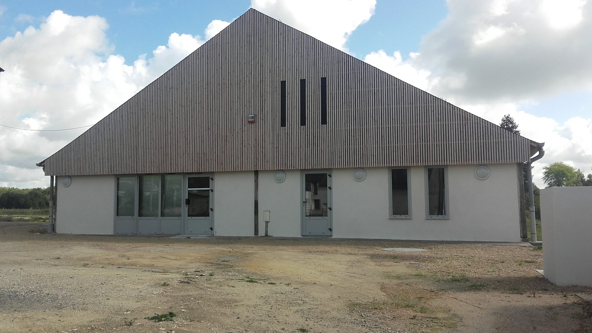 Bâtiment industriel avec toiture en tôle ondulée, fenêtres et portes en métal.