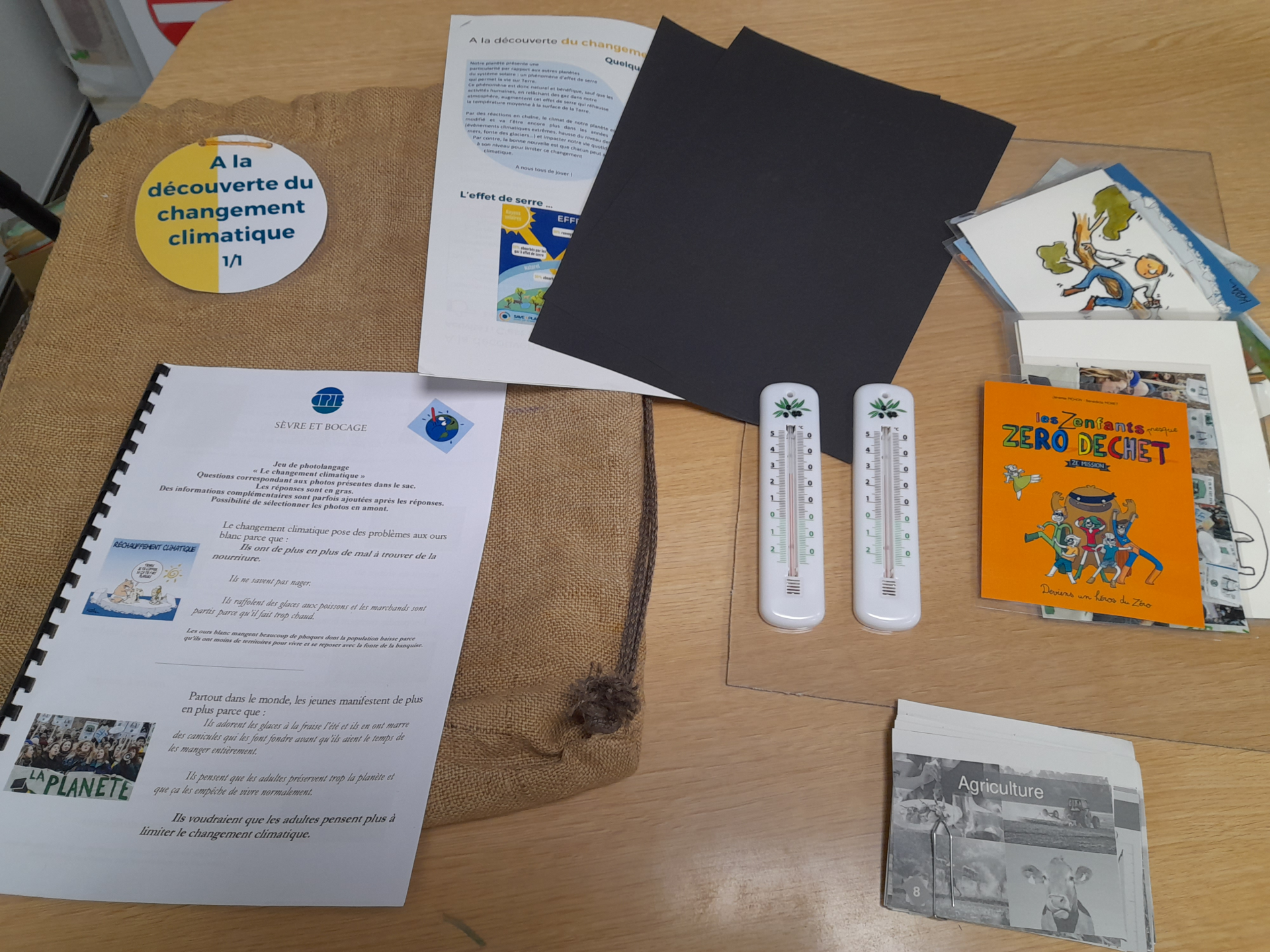 Sur une table, divers documents et objets liés au changement climatique. Inclut un badge, des brochures, un livre, des thermomètres et des feuilles imprimées.