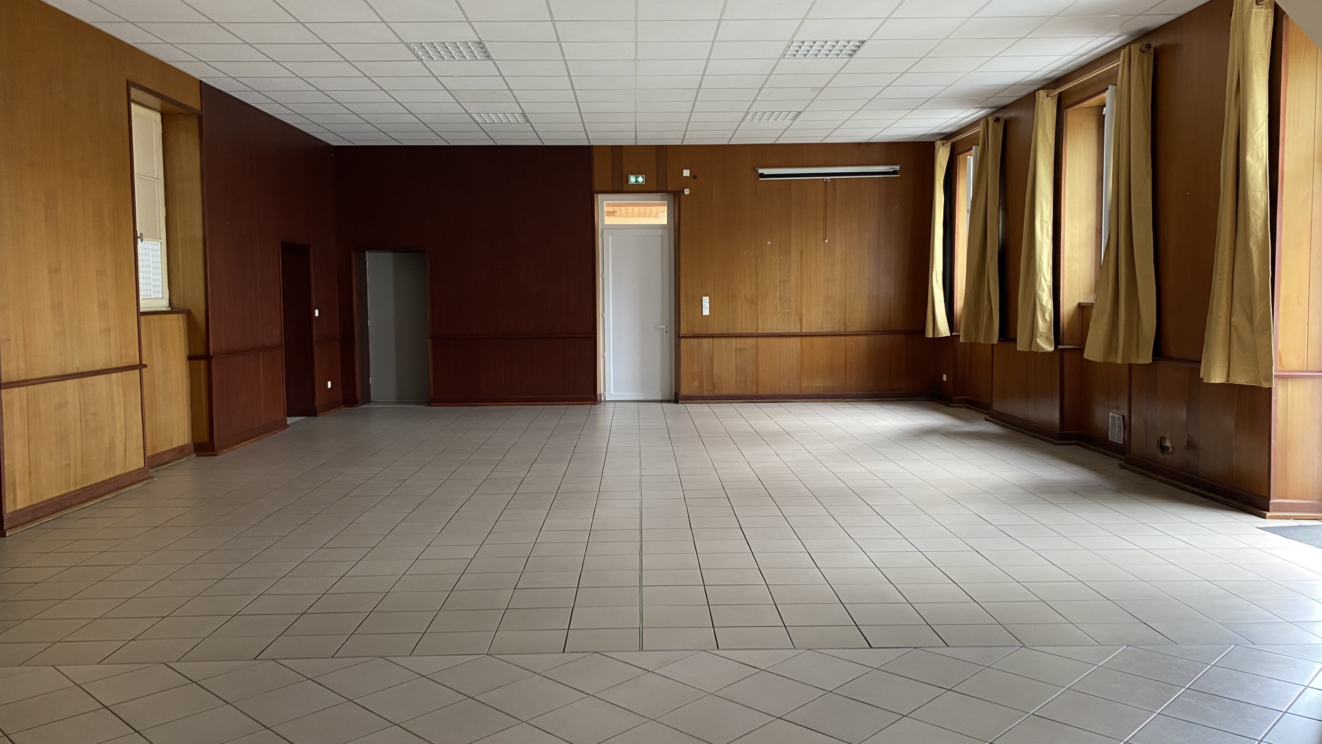 Pièce vide avec sol carrelé, murs en bois, porte et fenêtres avec rideaux.