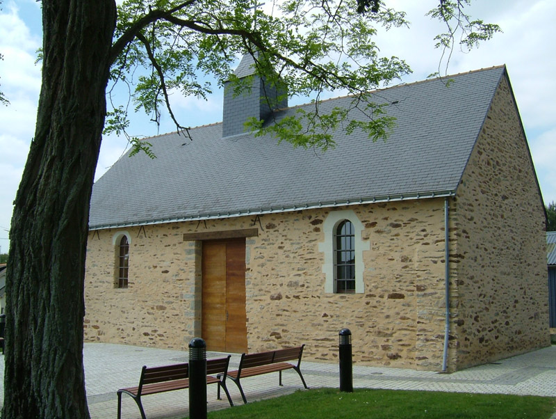 Bâtiment en pierre avec porte en bois, banc et poubelle devant.
