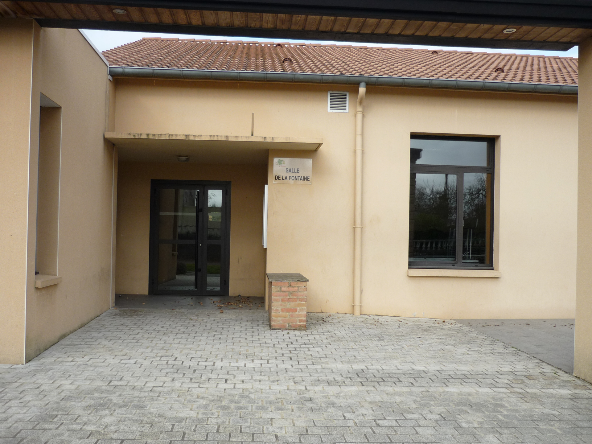 Entrée d'un bâtiment avec porte, fenêtres et panneau indiquant la salle de la fontaine.