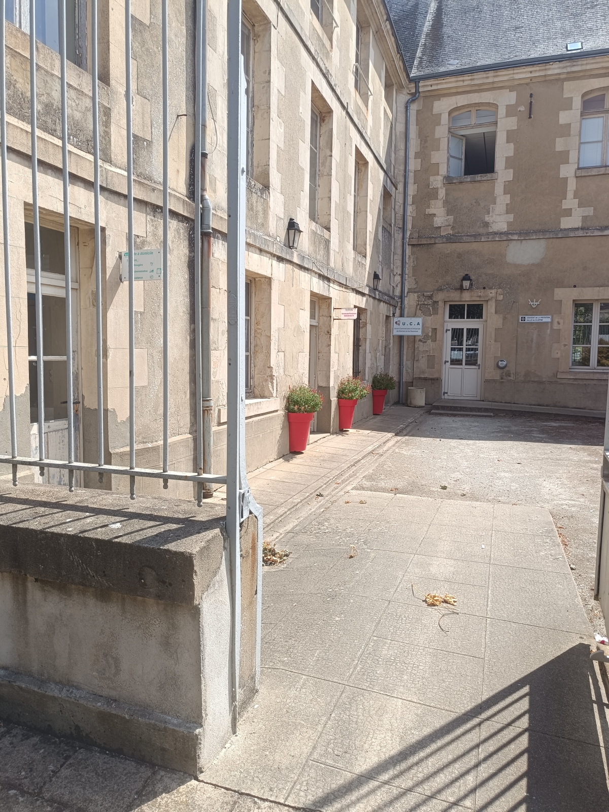 Cour intérieure avec bâtiments, portes, fenêtres, pots de fleurs et bancs.
