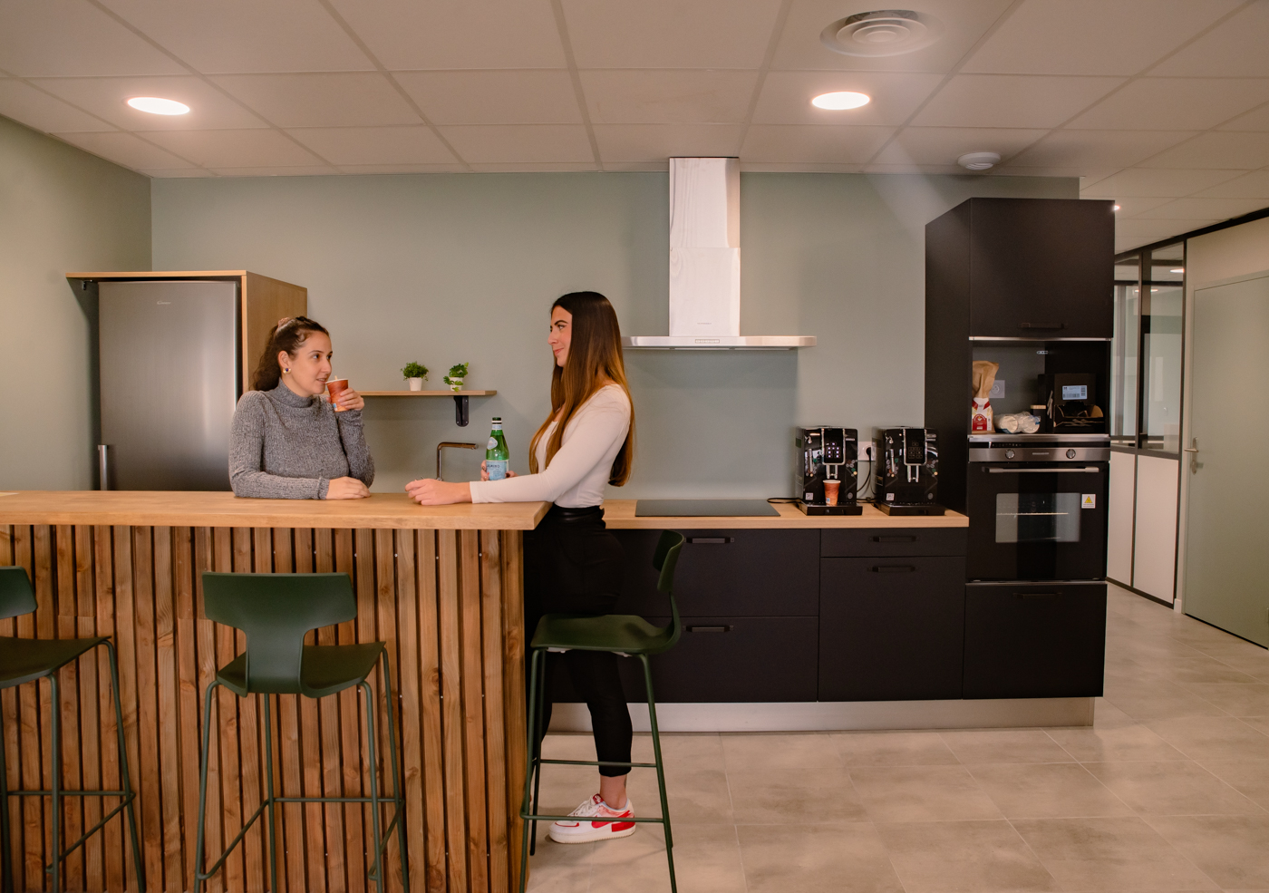 Cuisine avec comptoir, tabourets, réfrigérateur, four, et hotte aspirante.