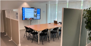 Salle de réunion avec table, chaises, écran, vidéoprojecteur, ordinateur portable et paravents.