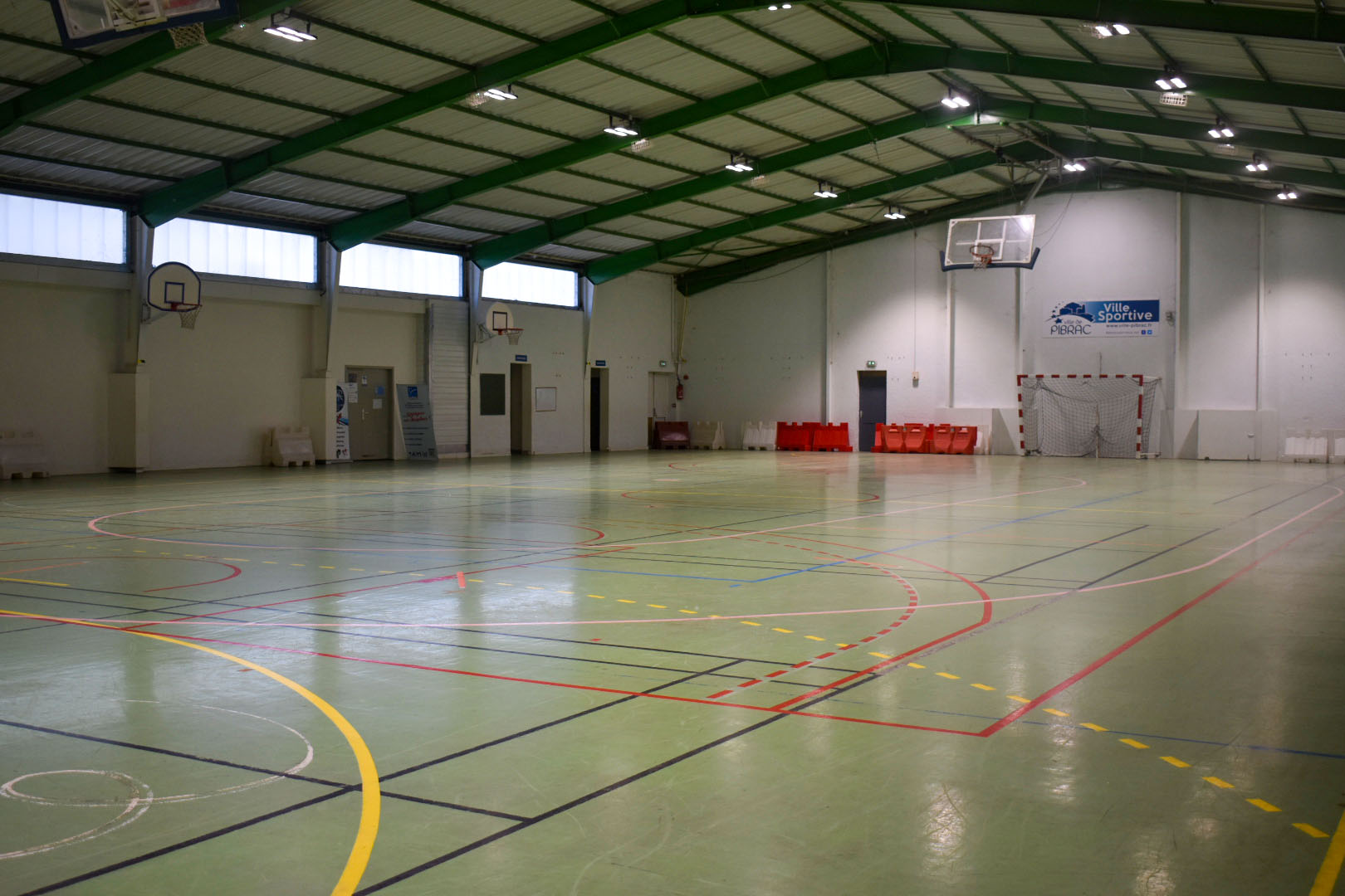 Salle de sport avec paniers, enclos de handball, lignes de sol, escaliers, et portes.