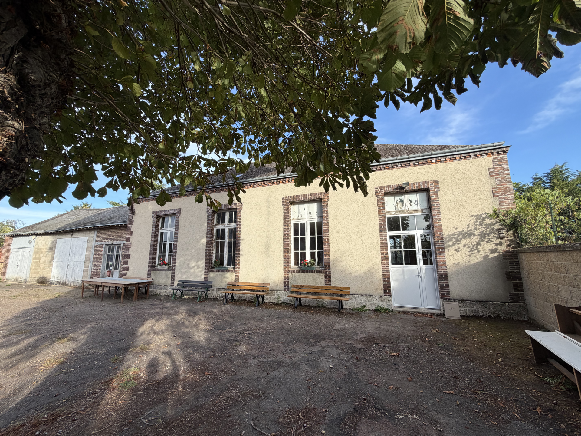 Bâtiment avec fenêtres, portes, bancs et tables en extérieur.