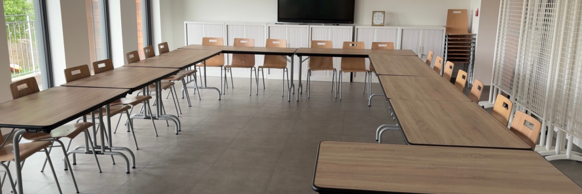 Salle de classe avec tables, chaises, écran et porte-manteau.