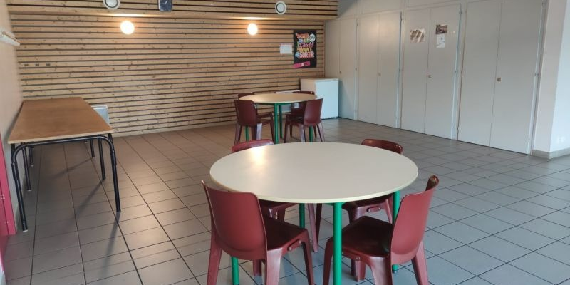 Salle avec tables rondes, chaises, tableau et armoires.